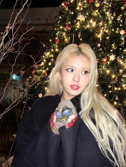 Somi mengenakan coat hitam dengn glove knit coklat motif bunga saat berfoto di depan pohon Natal yang cukup besar. [@somisomi0309]