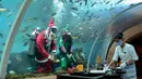 Penyelam yang mengenakan pakaian Sinterklas dan peri menyaksikan seorang pelayan menata meja dari akuarium di Koral Restaurant, Sawangan, Nusa Dua, Bali, Kamis (23/12/2021). Koral Restaurant dikenal sebagai restoran akuarium pertama di Pulau Dewata. (SONY TUMBELAKA/AFP)