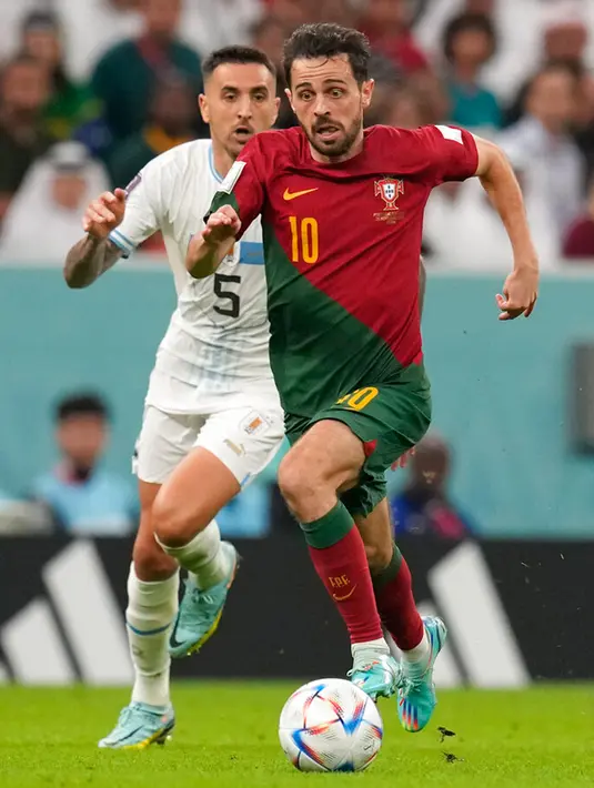 Pemain Uruguay Matias Vecino (kiri) berebut bola dengan pemain Portugal Bernardo Silva pada pertandingan sepak bola Grup H Piala Dunia 2022 di Stadion Lusail, Lusail, Qatar, 28 November 2022. Portugal mengalahkan Uruguay dengan skor 2-0. (AP Photo/Themba Hadebe)