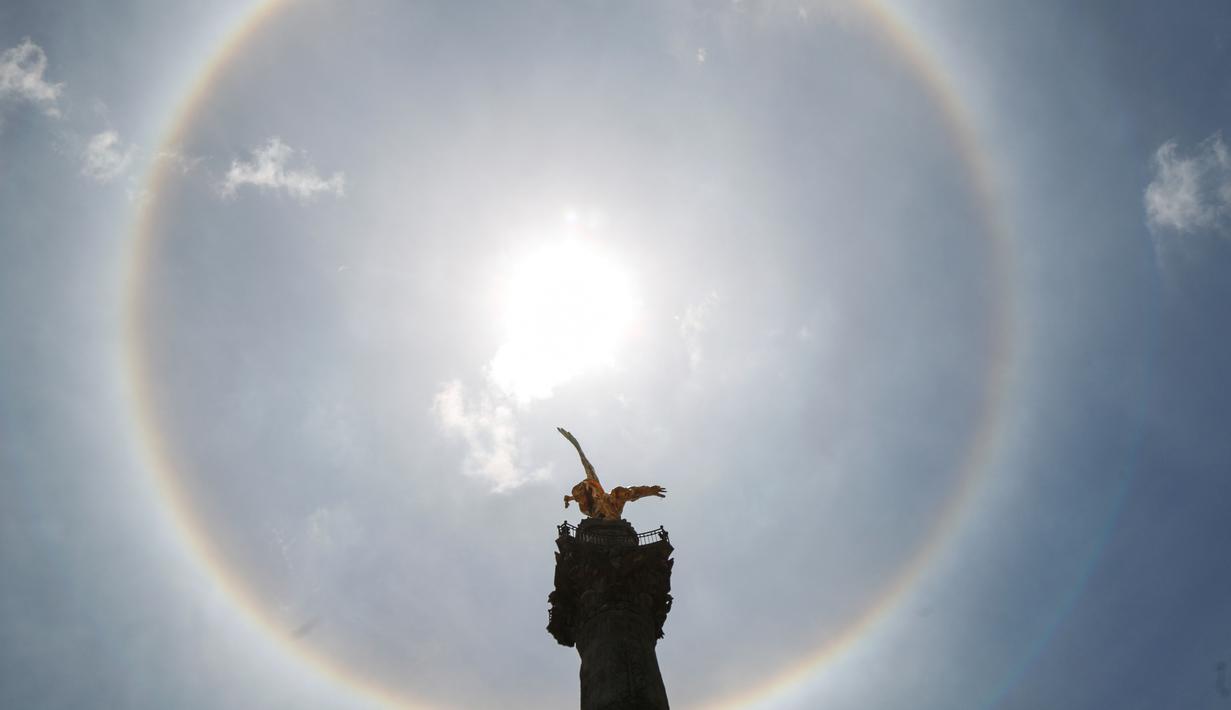 Fenomena halo matahari dengan latar depan monumen Malaikat Kemerdekaan di pusat kota Mexico City, Sabtu (7/7). Fenomena halo matahari terjadi karena pembiasan kristal es yang berada di sekitar Matahari yang membentuk semacam pelangi. (AP/Anthony Vazquez)