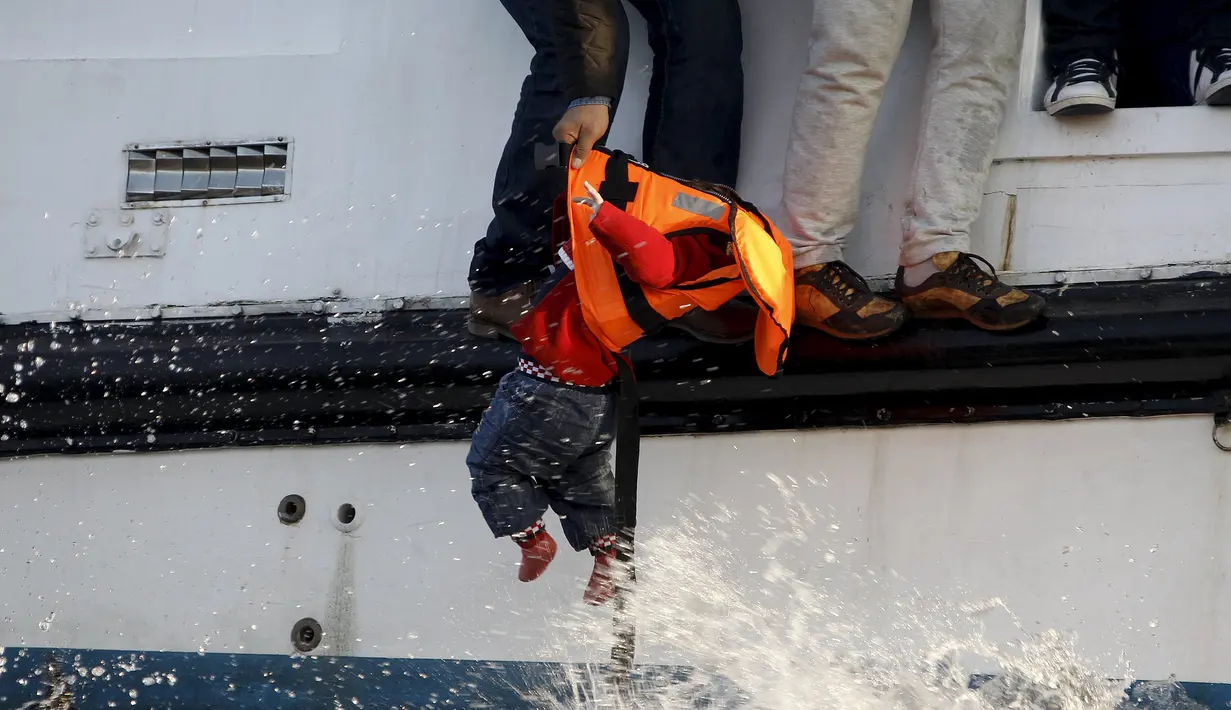 Seorang Imigran saat akan menyerahkan  bayi untuk diselamatkan oleh petugas karena perahu yang ditumpangi mereka akan karam di Laut Aegea, Yunani, 30 Oktober 2015. (REUTERS/Giorgos Moutafis)