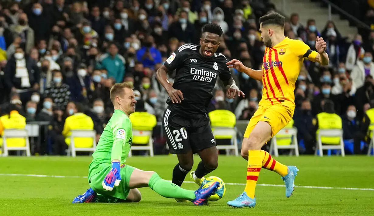 Penjaga gawang Barcelona Marc-Andre ter Stegen (kiri) melakukan penyelamatan di depan pemain Real Madrid Vinicius Junior (tengah) pada pertandingan sepak bola La Liga Spanyol di Stadion Santiago Bernabeu, Madrid, Spanyol, Minggu (20/3/2022). Barcelona menang 4-0. (AP Photo/Manu Fernandez)