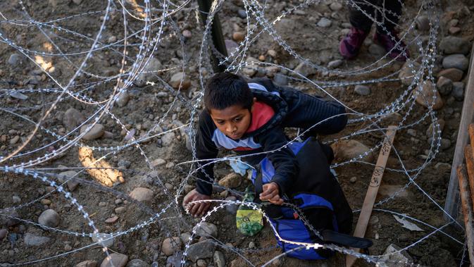 Kevin Andres, seorang anak imigran Meksiko berusaha melewati kawat berduri untuk masuk ke perbatasan (28/12). Aksi imigran ilegal ini dilakukan demi bisa menembus perbatasan AS yang semakin ketat. (AP Photo/Daniel Ochoa de Olza)