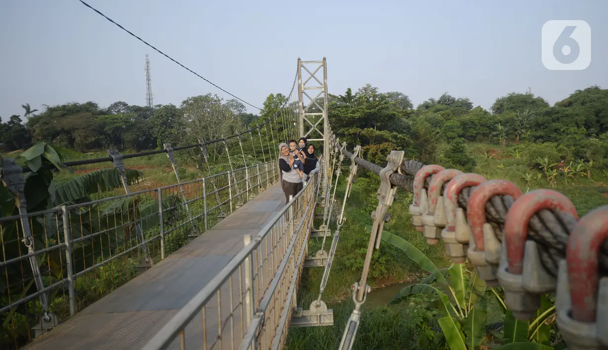 Warga melintasi jembatan gantung di Kelurahan Curug, Bojongsari, Kota Depok, Jawa Barat, Senin (24/8/2020). Setiap sore, warga sekitar bermain di jembatan tersebut sambil menikmati matahari tenggelam. (merdeka.com/Dwi Narwoko)