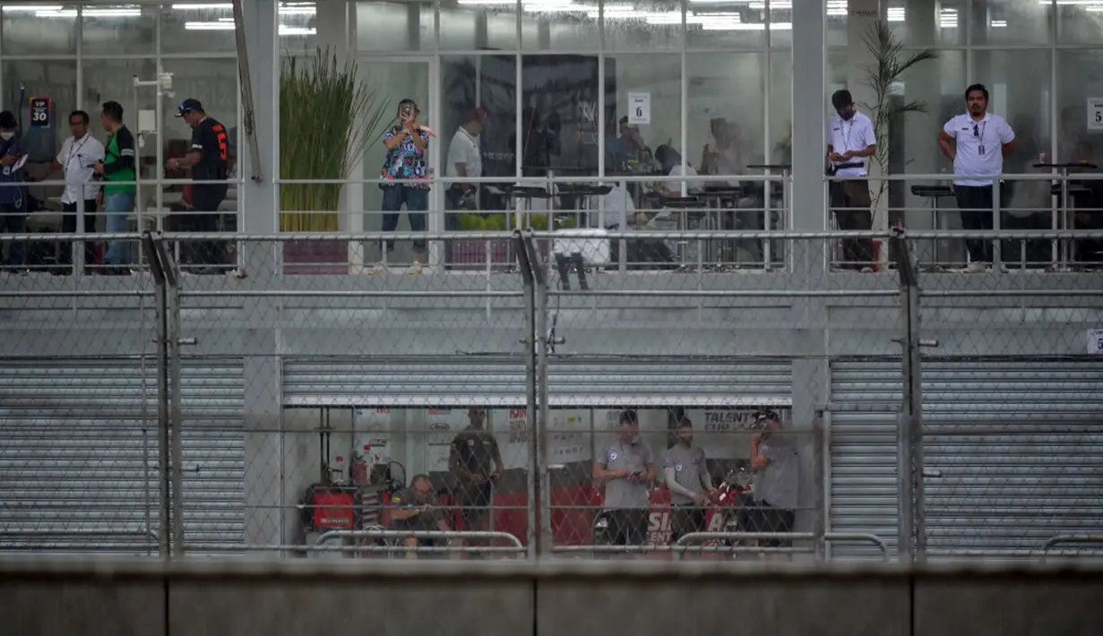 Personel tim, ofisial, dan peserta menyaksikan hujan deras yang menyebabkan penundaan Race 1 World Superbike (WSBK) di Pertamina Mandalika International Street Circuit, Lombok Tengah, Nusa Tenggara Barat, Sabtu (20/11/2021). Race 1 WSBK Mandalika ditunda pada 21 November. (BAY ISMOYO/AFP)