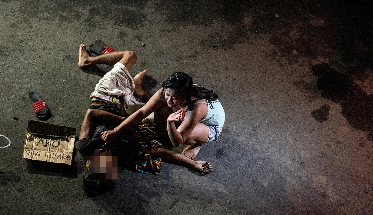 Foto yang diambil pada 23 Juli 2016 menunjukkan Jennilyn Olayres (kanan) menangisi jasad suaminya yang tewas ditembak orang tak dikenal dan terkapar di samping karton bertuliskan “Saya bandar” di sebuah jalan di Manila, Filipina. (AFP PHOTO/Noel CELIS)