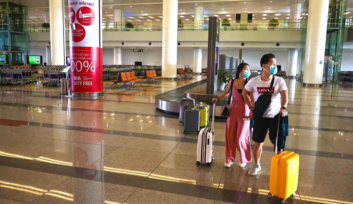 <p>Penumpang dengan mengenakan masker berjalan membawa barang mereka di terminal kedatangan Bandara Internasional Noi Bai yang kosong di Hanoi, Vietnam, Kamis (27/2/2020). Jumlah penumpang pesawat menurun di tengah ancaman infeksi virus corona yang bernama resmi COVID-19. (Mladen ANTONOV/AFP)</p>