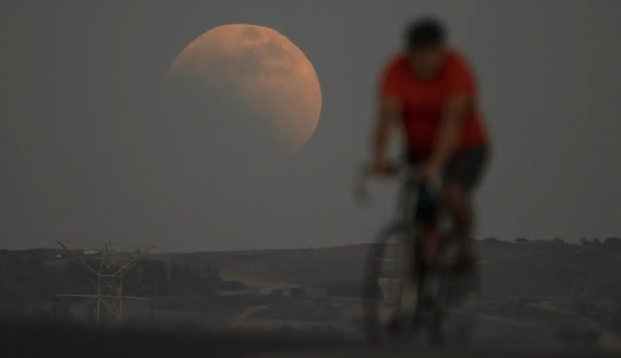 Gerhana bulan terlihat di belakang pengendara sepeda saat blood moon pertama tahun ini di Irwindale, California, Amerika Serikat, Minggu (15/5/2022). (AP Photo/Ringo H.W. Chiu)