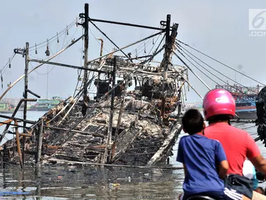 Pengendara sepeda motor melintas dekat kapal yang ludes dilalap api di Pelabuhan Muara Baru, Jakarta, Minggu (24/2). Sebanyak 18 unit kapal tradisional hangus akibat kebakaran pada Sabtu, 23 Februari 2019. (Merdeka.com/Iqbal Nugroho)