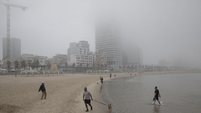 Orang-orang berjalan di pantai saat hari berkabut di Tel Aviv, Israel, Rabu (6/1/2021). Kondisi ini disinyalir dapat mengaburkan jarak pandang dan memperlambat lalu lintas. (AP Photo/Oded Balilty)