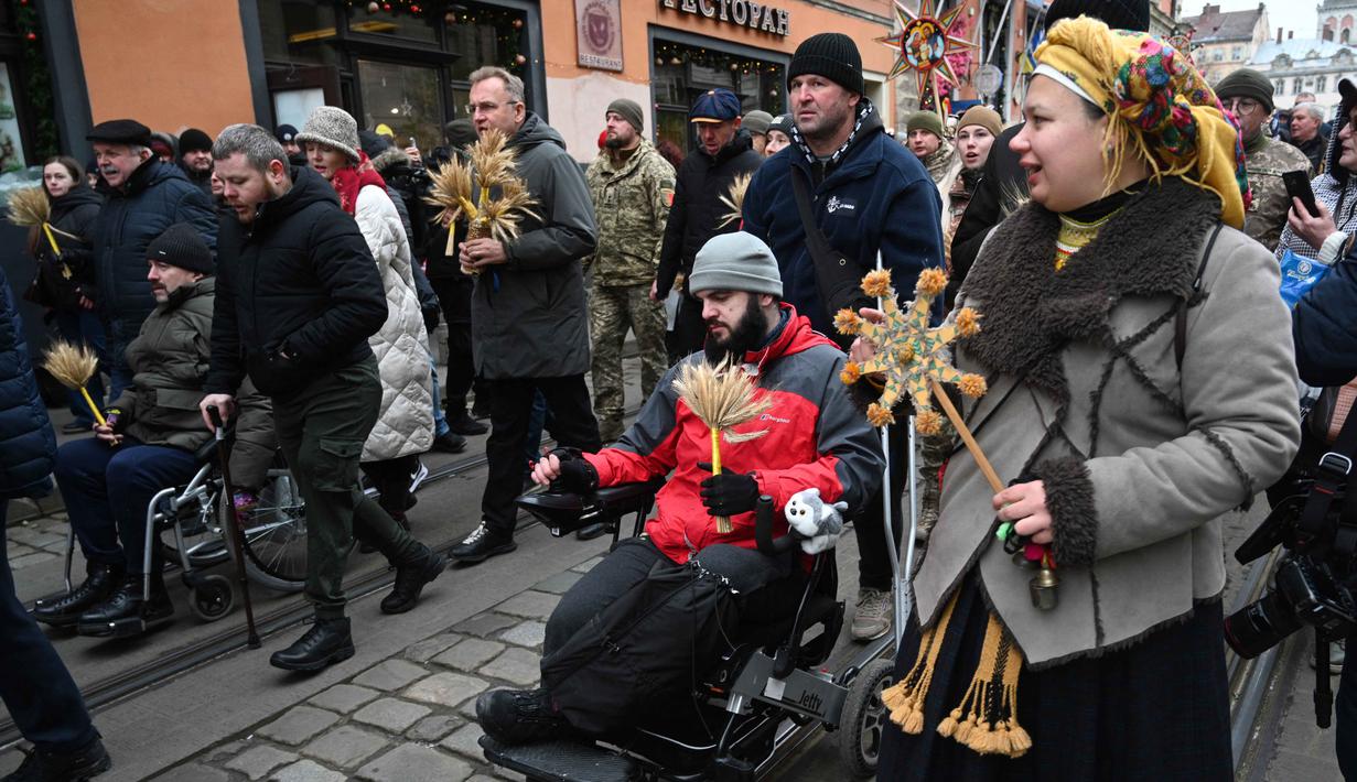 Seringkali 'Didukh' berfungsi sebagai pengganti pohon Natal dan menjadi pusat perayaan. Tampak dalam foto, para veteran Ukraina yang terluka memegang hiasan tradisional 'Didukh' saat mereka mengikuti prosesi Malam Natal di Lviv pada 24 Desember 2025. (YURIY DYACHYSHYN/AFP)