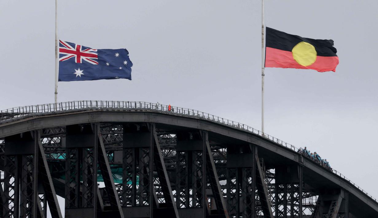 Sebagai informasi, penembakan ini terjadi di tengah aturan ketat pemerintah Australia terkait undang-undang kepemilikan senjata api, terutama sejak tragedi Port Arthur pada 1996. Tampak dalam foto, bendera Australia dan Aborigin dikibarkan setengah tiang di Jembatan Pelabuhan Sydney setelah penembakan di Pantai Bondi, Sydney pada 15 Desember 2025. (DAVID GRAY/AFP)