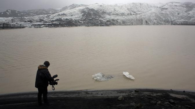 Kameraman mengambil gambar bongkahan es yang terapung di perairan Gletser Solheimajokull, Islandia, Jumat (16/10). Pemanasan global menyebabkan gletser Solheimajokull mencair hingga 1 km sejak pengukuran tahunan pada 1931. (AFP PHOTO/POOL/Thibault Camus)