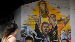 Warga melihat Mural yang menggambarkan kapten dan penyerang Argentina Lionel Messi mengangkat Trofi Piala Dunia 2022 di samping rekan satu timnya setelah memenangkan turnamen Piala Dunia Qatar 2022 di Buenos Aires pada 22 Desember 2022. Argentina berhasil meraih juara setelah mengalahkan Prancis di babak final. (AFP/Luis Robayo)