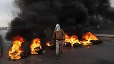 Seorang pengunjuk rasa melewati ban yang terbakar di sepanjang jalan raya utama yang mengarah ke Bandara Internasional Beirut selama protes terhadap kenaikan harga barang-barang konsumen dan jatuhnya mata uang lokal di Beirut, Lebanon, Senin (29/11/2021). (AP Photo/Hussein Malla)