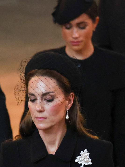 Kate Middleton dan Meghan Markle berjalan saat mengikuti prosesi persemayaman Ratu Elizabeth II di Westminster Hall di London (14/9/2022). Meghan dan Kate punya cara tersendiri untuk menunjukkan rasa hormat kepada mendiang Ratu Elizabeth II, keduanya mengenakan perhiasan yang bermakna spesial, karena diberikan oleh sang nenek mertua. (AFP/Pool/Phil Nolbe)