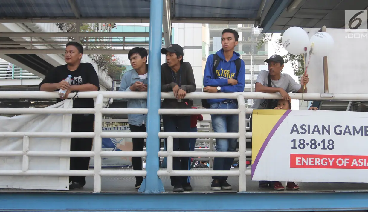 Warga menyaksikan Parade Asian Games 2018 2018 yang melintas dari atas JPO di Jalan Thamrin, Jakarta, Minggu (13/5). Parade Asian Games 2018 jadi pusat perhatian pengunjung Car Free Day. (Liputan6.com/Arya Manggala)