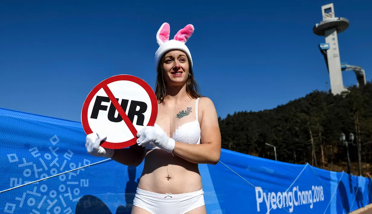 Seorang aktivis wanita dari PETA berunjuk rasa di samping spanduk Olimpiade Pyeongchang 2018 di Pyeongchang, Korea Selatan (6/2). Aktivis ini nekat tampil berbikini saat unjak rasa berlangsung. (AFP Photo/Dimitar Dilkoff)