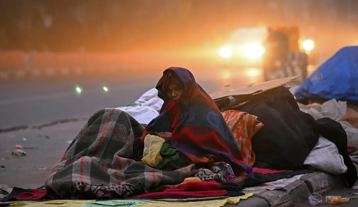 Seorang wanita tunawisma terbungkus selimut duduk di pinggir jalan pada pagi musim dingin yang dingin di New Delhi, India, Selasa (2/1/2024). (Money SHARMA / AFP)