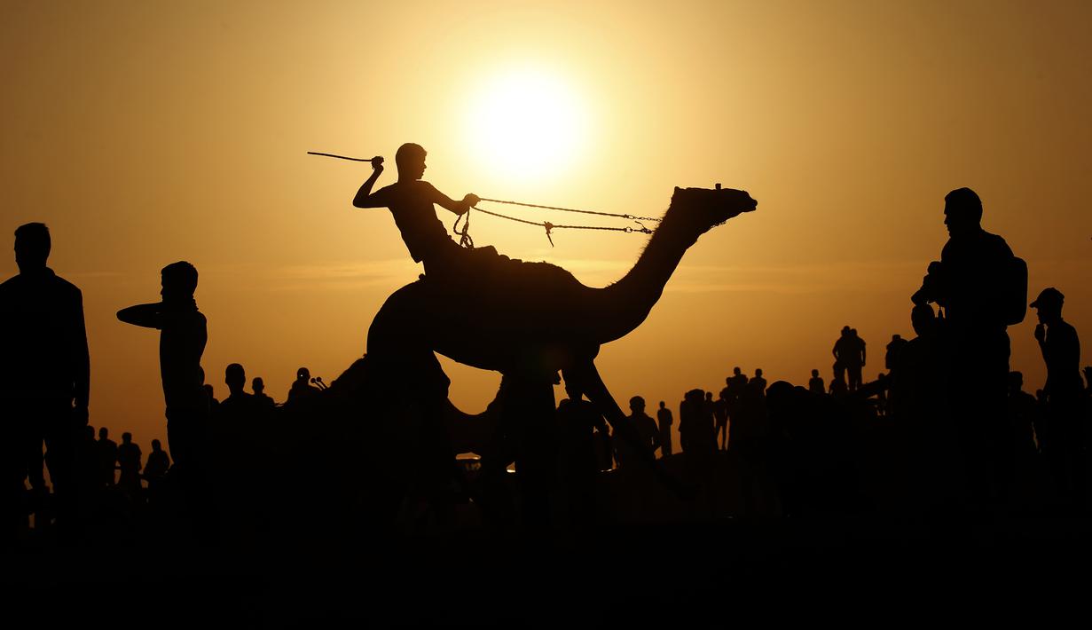 Seorang joki Palestina beraksi saat bersaing dalam perlombaan unta lokal yang diadakan di lokasi bekas bandara Gaza yang hancur, di Rafah, Jalur Gaza selatan (20/10/2019). Bandara Internasional Yasser Arafat yang diresmikan November 1998, kini tinggal reruntuhan akibat serangan Israel. (AFP Photo/Sa