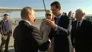 Presiden Suriah Bashar Assad bersalaman dengan Presiden Rusia, Vladimir Putin saat tiba di pangkalan udara Hemeimeem di Suriah (11/12). Putin menyatakan akan menarik pasukan Rusia di Suriah. (Presidential TV photo via AP)