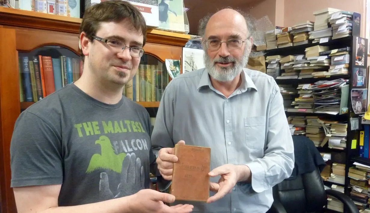 Richard Sprent, pemilik toko buku bekas (kiri) memperlihatkan sebuah buku berusia 200 tahun yang diduga berasal dari jaman Perang Napoleon di toko buku miliknya, di Hobart, ibu kota negara bagian Tasmania, Australia, Selasa (10/5). (STR/AFP)