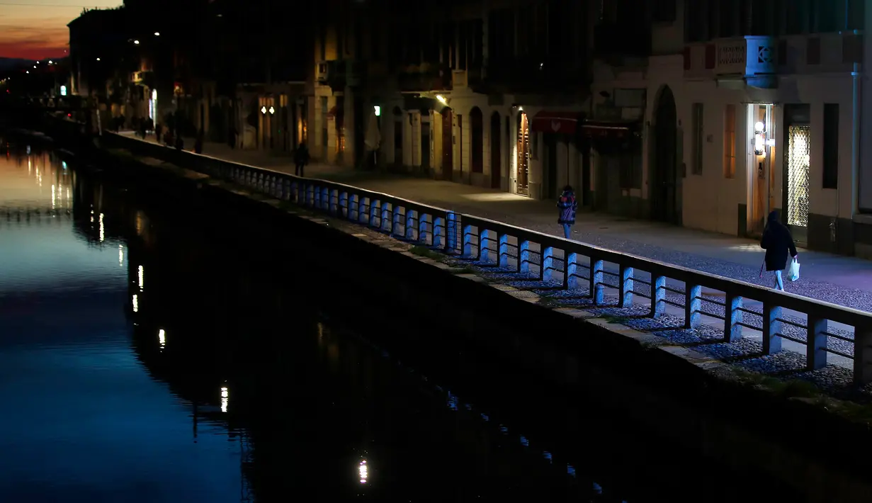 Beberapa orang berjalan di Kanal Naviglio Grande, Milan, Italia, Selasa (10/3/2020). Merebaknya virus corona (COVID-19) membuat pemerintah Italia membatasi bepergian, melarang berkumpul di tempat umum, menutup tempat publik, hingga meliburkan sekolah. (AP Photo/Antonio Calanni)