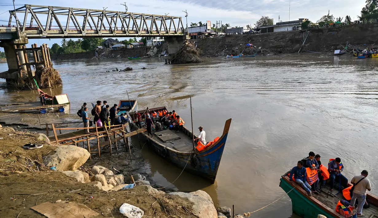 Untuk sementara, warga terpaksa menggunakan perahu nelayan sebagai sarana penyeberangan darurat di sungai. Tampak dalam foto, para penumpang menaiki perahu untuk menyeberangi Sungai Peusangan di Kuta Blang, Kabupaten Bireuen, Provinsi Aceh, pada Selasa 9 Desember 2025. (CHAIDEER MAHYUDDIN/AFP)