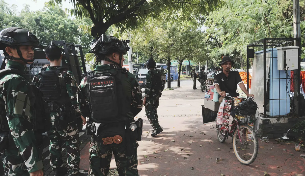 Seorang penjual minuman bersepeda melintas di depan personel Tentara Nasional Indonesia (TNI) yang berjaga di sebuah jalan setelah beberapa hari terjadi aksi unjuk rasa menentang kenaikan tunjangan anggota Dewan Perwakilan Rakyat (DPR), di Jakarta, Senin 1 September 2025. (AP Photo/Tatan Syuflana)