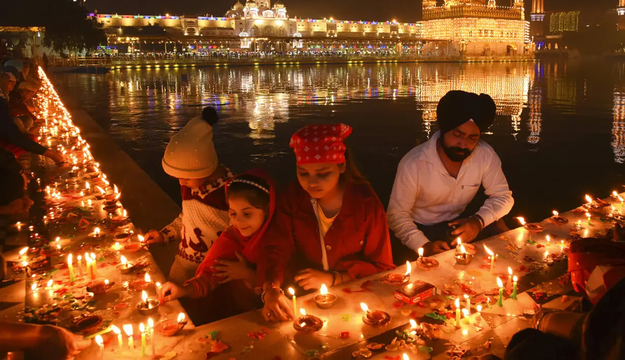 Umat Sikh menyalakan lampu tanah di Kuil Emas yang diterangi pada peringatan kelahiran Guru Nanak di Amritsar, India, 19 November 2021. Guru Nanak adalah Guru Sikh pertama dan pendiri Sikhisme. (AP Photo/Prabhjot Gill)