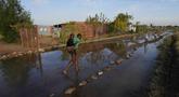 Gadis muda menggendong seorang anak di punggungnya melalui jalan yang tergenang banjir di dekat waduk yang meluap di Hamanskraal, Pretoria, Afrika Selatan, Jumat, 26 Mei 2023. (AP Photo/Themba Hadebe)