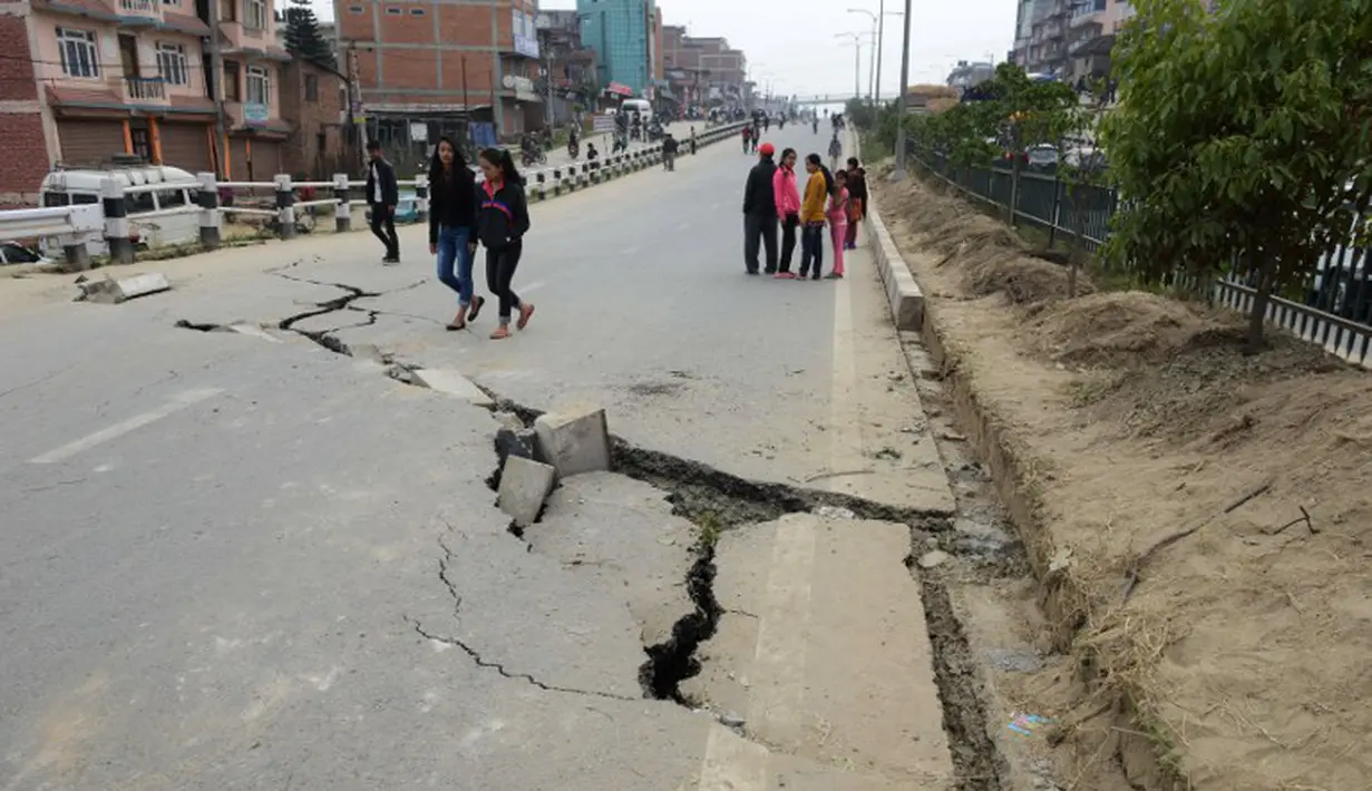 Sejumlah warga di Kathmandu berjalan melintasi jalan yang rusak akibat gempa , Minggu (26/4/2015). Gempa berkekuatan 7,8 Skala Richter dikabarkan telah menelan korban sekitar 2000 jiwa. (AFP Photo/Prakash Mathema)