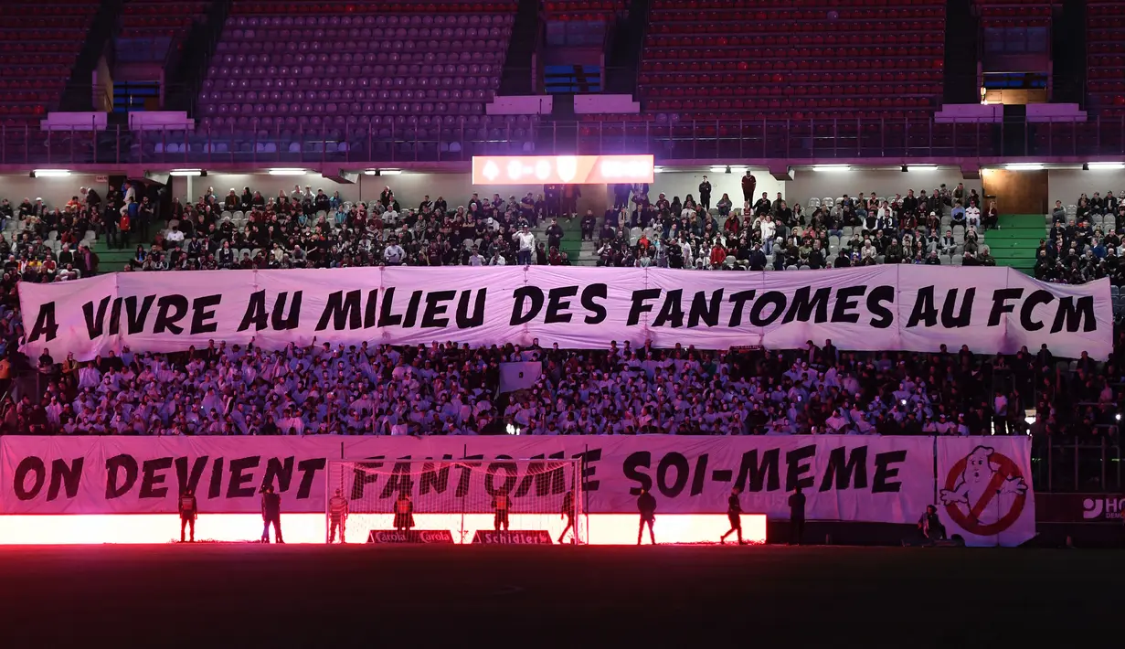 Suporter FC Metz membentangkan spanduk bertulisakan "Saat Anda hidup bersama hantu FC Metz, Anda sendirilah yang menjadi hantu" pada laga lanjutan Liga Prancis 2023/2024 melawan RC Lens di Saint-Symphorien Stadium, Longeville-les-Metz, Prancis, Sabtu (13/04/2024) dini hari WIB. (AFP/Jean-Christophe Verhaegen)