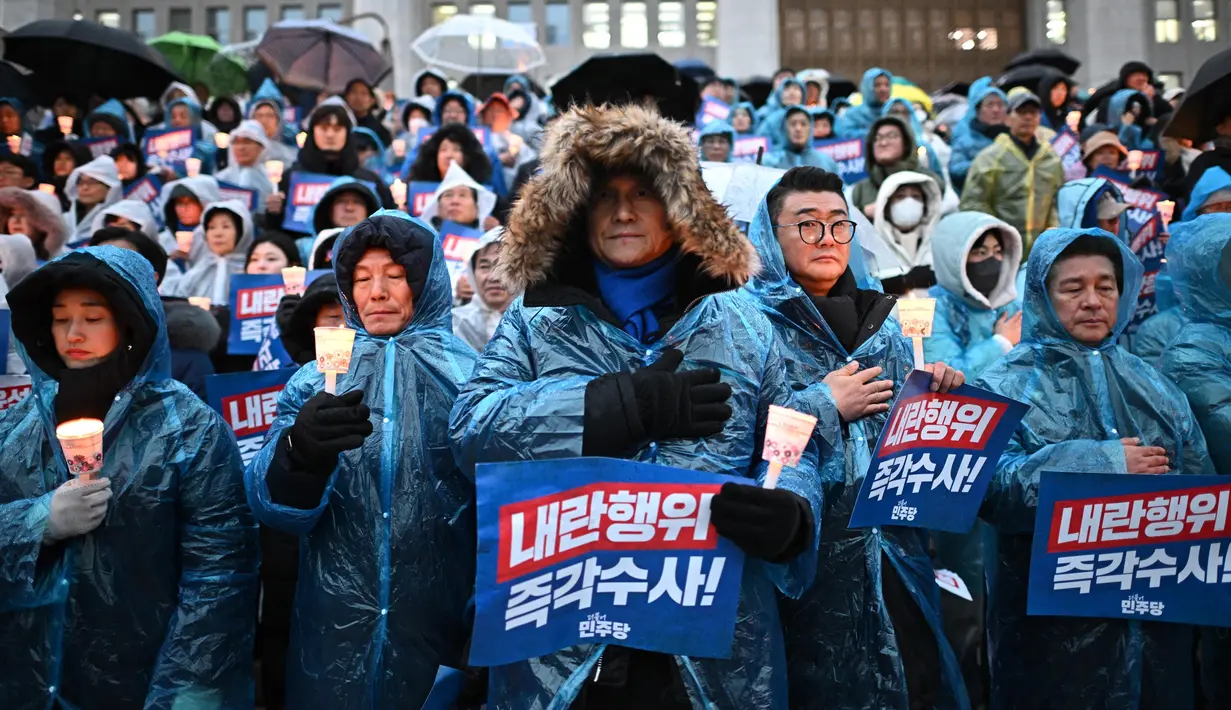 Para pengunjuk rasa mengenakan ponco di tengah hujan saat mereka mengambil bagian dalam aksi menyalakan lilin yang menyerukan penggulingan Presiden Korea Selatan Yoon Suk Yeol di tangga Majelis Nasional di Seoul pada Kamis 5 Desember 2024. (Philip FONG/AFP)