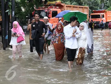 Pengantin Mansur dan Maya melintasi banjir usai melakukan akad nikah di KUA Mampang Prapatan, Jakarta, Selasa (21/2). Walapun banjir sepasang pengantin ini tetap melakukan akad nikah. (Liputan6.com/Herman Zakharia)