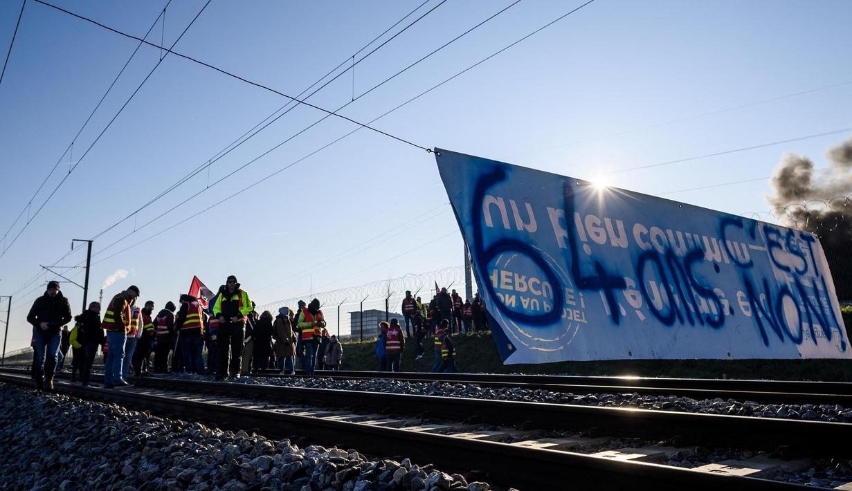 Puluhan pekerja berdiri di rel kereta api di belakang spanduk bertuliskan "64 tahun, tidak" dalam sebuah aksi yang diserukan oleh serikat pekerja Prancis, Konfederasi Umum Buruh (CGT), untuk memprotes perombakan pensiun di Donges, Prancis Barat, Rabu (8/2/2023). Prancis bersiap menghadapi pemogokan baru dan demonstrasi massal menentang proposal Presiden Prancis untuk mereformasi pensiun Prancis, termasuk menaikkan usia pensiun dari 62 menjadi 64 tahun. (LOIC VENANCE/AFP)