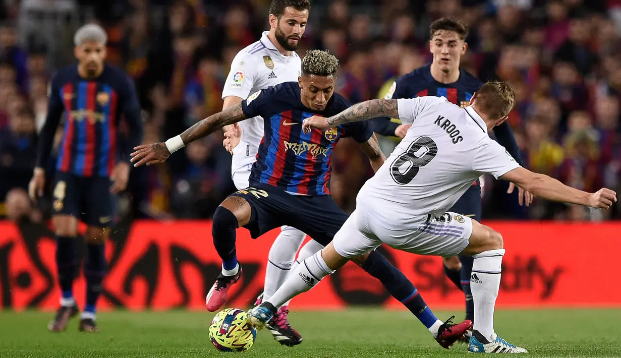Pemain Barcelona, Raphinha (tengah) berusaha melewati pemain Real Madrid pada laga pekan ke-26 Liga Spanyol 2022/2023 di Camp Nou, Barcelona, Senin (20/03/2023). Blaugrana menang dengan skor 2-1 pada pertandingan yang bertajuk El Classico tersebut. (AFP/Josep Lago)