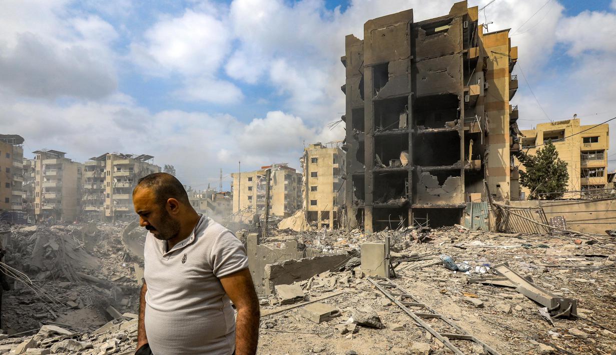 Seorang pria berjalan melewati sebuah lubang di mana sebuah bangunan yang runtuh berdiri setelah serangan udara Israel semalam di lingkungan Kafaat di pinggiran selatan Beirut, pada 7 Oktober 2024. (Foto oleh AFP)