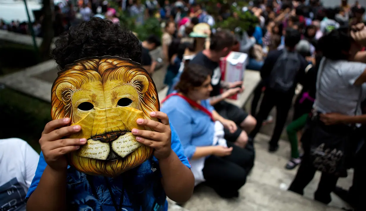 Seorang anak mengenakan topeng Cowardly Lion dari “The Wizard of Oz” lengkap dengan filter khusus dibagian lubang matanya saat menikmati gerhana matahari di Mexico City, Senin (21/8). (Rebecca Blackwell/AP)
