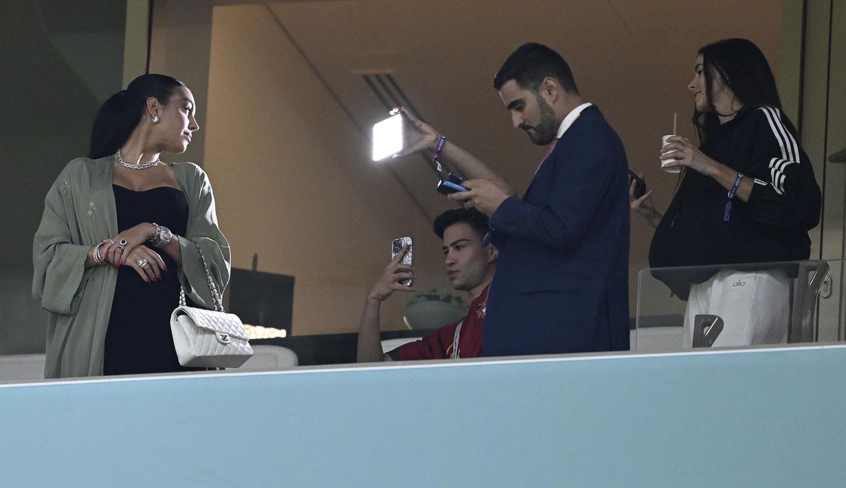 Georgina tampak glamor dengan mengenakan dress hitam dan mantel berwarna hijau sage. Ia juga melengkapi penampilannya dengan tas bermerk Chanel. (AFP/Patricia De Melo Moreira)