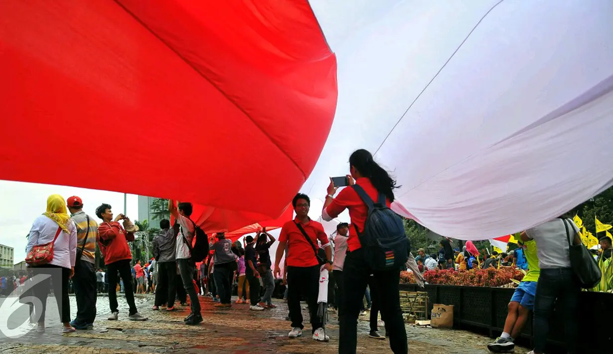 Seorang peserta 'Aksi Kita Indonesia' berfoto dibawah Bendera Merah Putih di Bundaran HI, Jakarta, Minggu (4/12). Ada banyak bendera Merah Putih dikibarkan oleh para peserta aksi hingga membuat Bundaran HI tampak memerah. (Liputan6.com/Angga Yuniar)