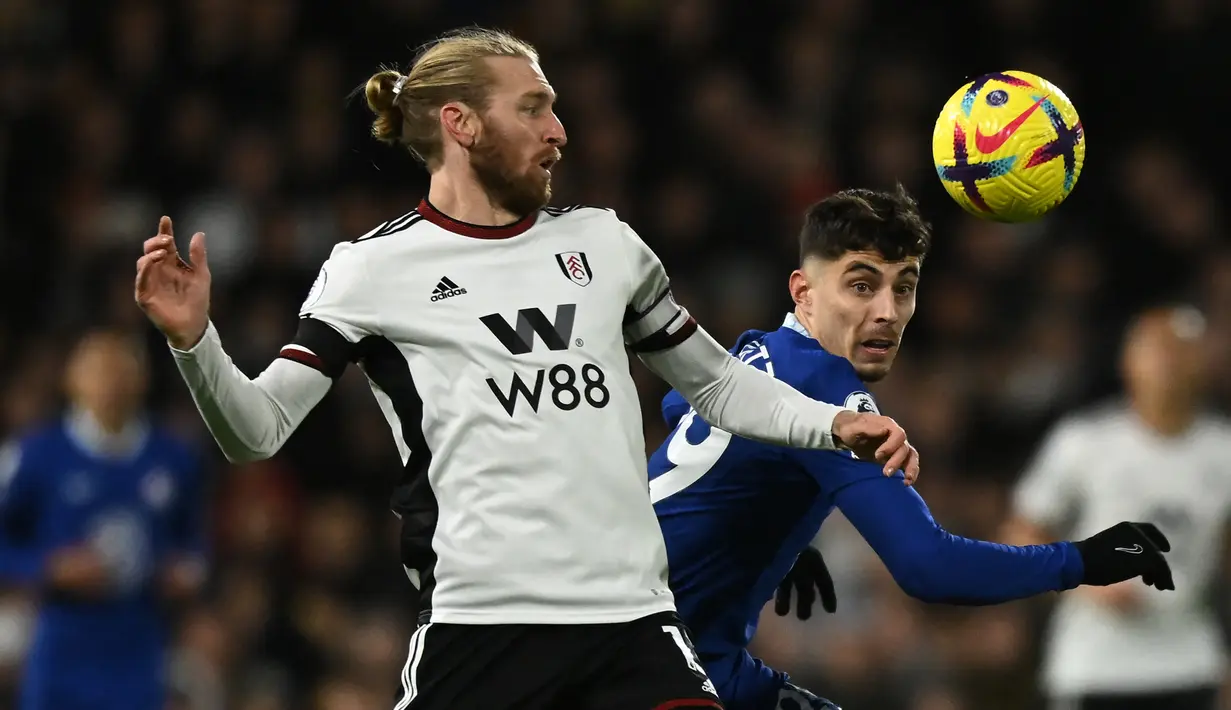 Bek Fulham Tim Ream (Kiri) berebut bola dengan gelandang Chelsea Kai Havertz pada laga tunda pekan ke-7 Premier League 2022/2023 di Craven Cottage, Jumat (13/1/2023) WIB. Selain kalah, Chelsea juga pulang dengan catatan negatif lainnya. (Ben Stansall / AFP)