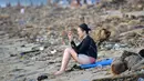 Seorang turis bermain ponsel dekat sampah yang terdampar akibat cuaca buruk di Pantai Kuta, Bali, Jumat (15/2). Hujan deras disertai angin kencang yang melanda Bali berdampak pada arus laut yang terus membawa sampah dari daerah lain. (SONNY TUMBELAKA/AFP)