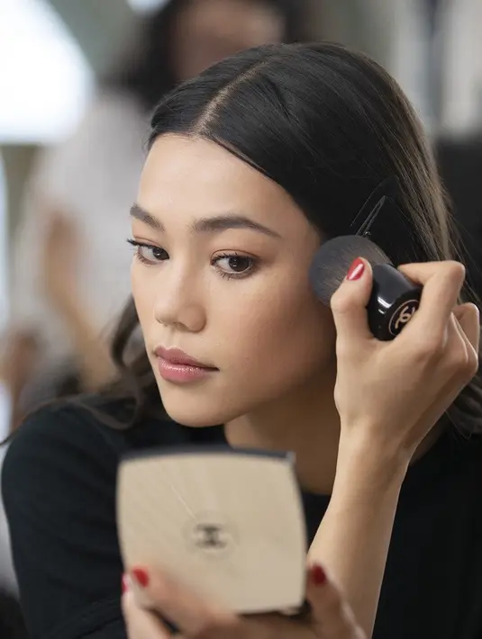<p>Model @nnguyenjade menyempurnakan pancarannya sebelum pertunjukan CHANEL Cruise 2022/23. Untuk melengkapi detail koleksi yang rumit, riasan dibuat sangat halus dengan kulit yang cerah, mata yang tegas, dan bibir yang kemerahan. (Dok/Chanel).</p>