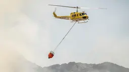 Sebuah helikopter membawa air untuk membantu memadamkan kebakaran yang melanda kawasan Somerset West dekat Cape Town, Afrika Selatan, Rabu (4/1). Kebakaran tersebut telah menghancurkan sebagian wilayah perkebunan tertua di Afsel. (AP Photo / Stefan Smuts)