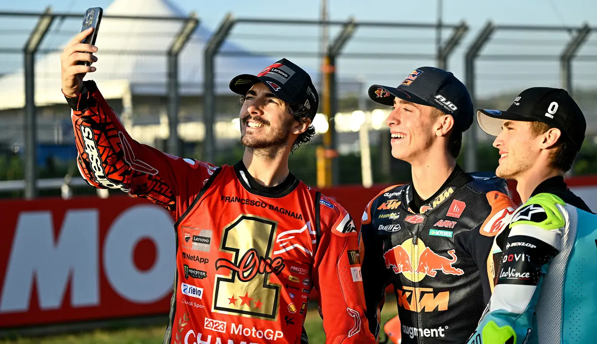 Pembalap Ducati Lenovo sekaligus juara dunia MotoGP 2023, Francesco Bagnaia (kiri), melakukan swafoto bersama juara Moto2 2023, Pedro Acosta (tengah), dan juara Moto3 Jaume Masia setelah ketiganya menyelesaikan rangkaian balapan di MotoGP Valencia, Minggu (26/11/2023). (AFP/Javier Soriano)