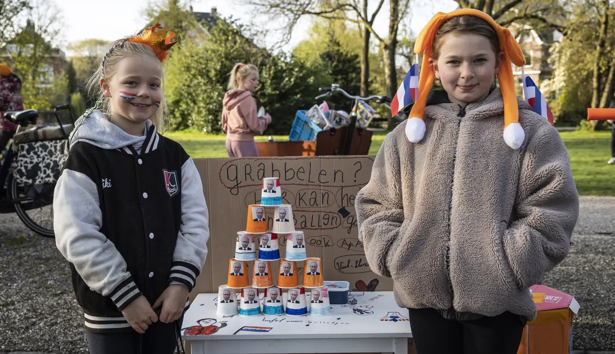 Anak-anak berpose di samping cangkir kertas sambil memajang gambar presiden Rusia Vladimir Putin yang dipajang di atas meja dalam acara perayaan Hari Raja di Vondelpark di Amsterdam, pada 27 April 2023. (Dingena Mol / ANP / AFP)