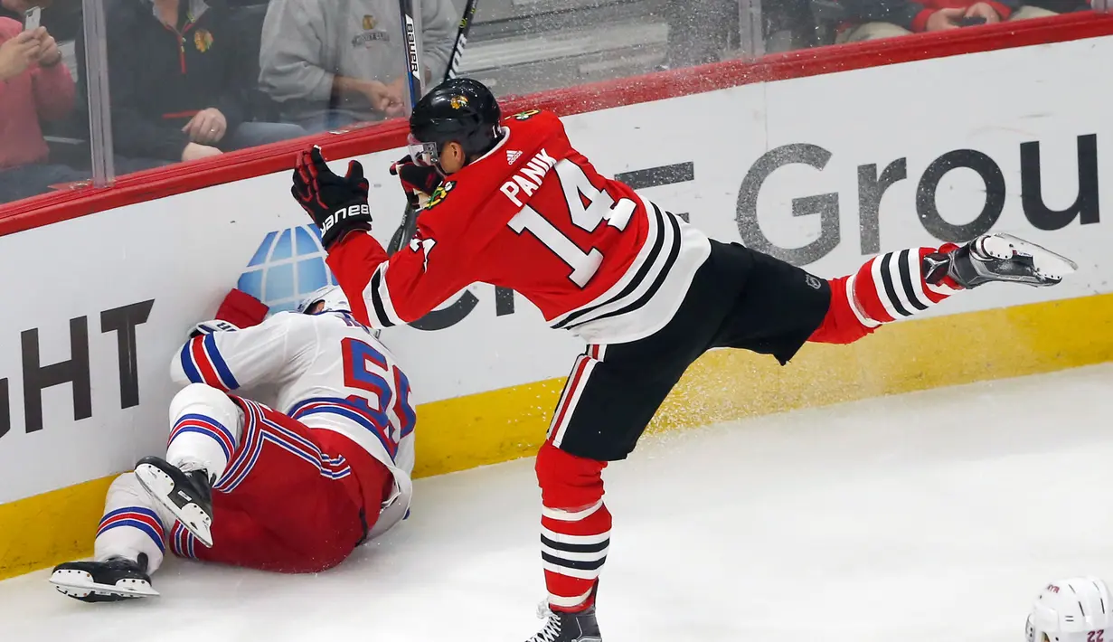 Pemain New York Rangers, Nick Holden terjatuh usai berebut puck dengan pemain Chicago Blackhawks Richard Panik saat pertandingan NHL di Chicago (15/11). Blackhawks unggul 6-3 atas Rangers. (AP/Charles Rex Arbogast)