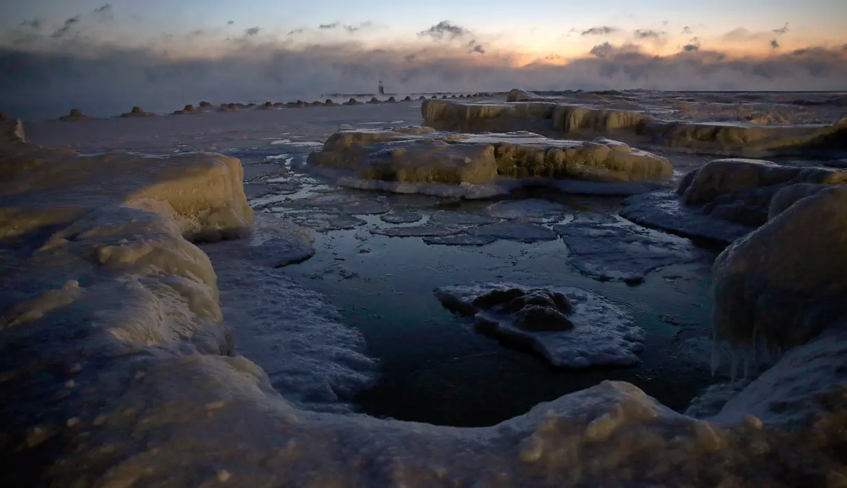 Lapisan es terbentuk di sepanjang pantai Danau Michigan sebelum matahari terbit di Chicago, Rabu (30/1). Dengan kondisi ini, suhu di Chicago, kota terbesar ketiga di AS, diperkirakan akan lebih dingin dari Antarktika di Kutub Selatan. (AP/Kiichiro Sato)