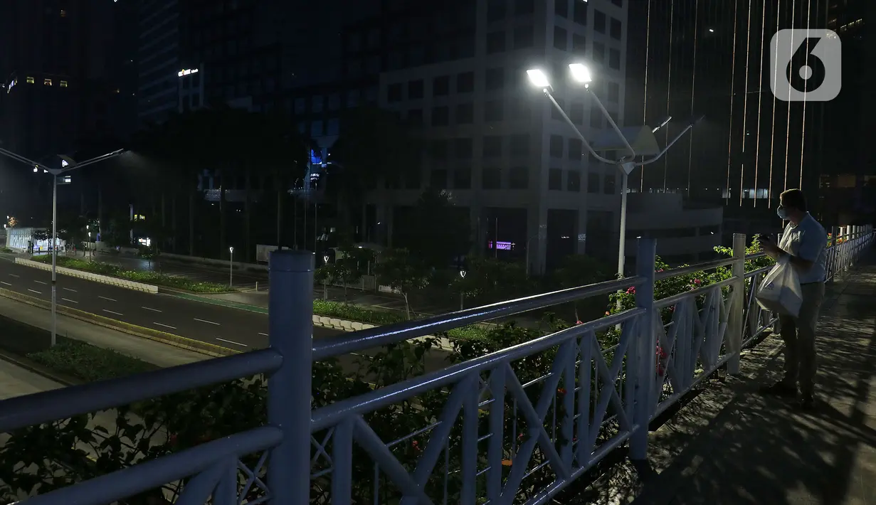 Warga melihat suasana jalan lengang kawasan Sudirman, Jakarta, Rabu (12/5/2021) malam. Polda Metro Jaya memberlakukan crowd free night untuk mencegah kerumunan takbir keliling di malam Idul Fitri 1442 yang berlaku mulai pukul 22:00 malam ini. (Liputan6.com/Herman Zakharia)